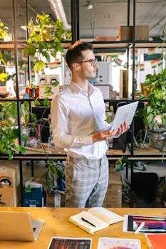 Caucasian man in corporate attire working on laptop in an indoor office with plants.