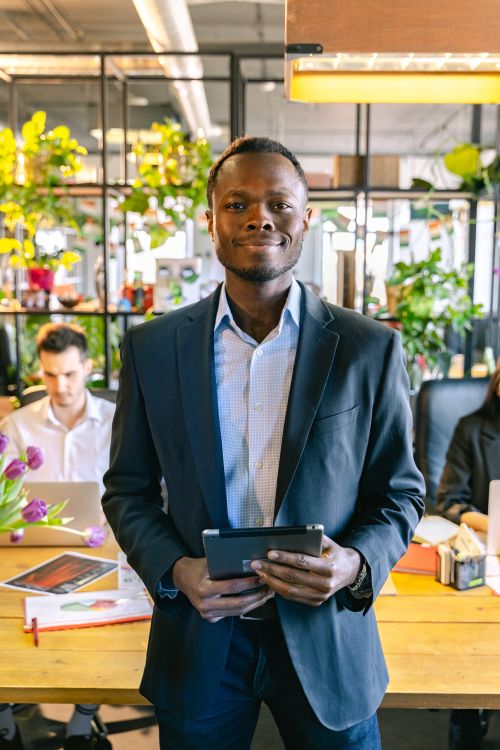 Free Confident adult man in a suit holding a tablet in a vibrant modern office setting. Stock Photo