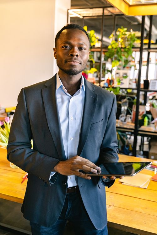 Free Young professional in a suit holds a tablet in a modern office, embodying business confidence and technology use. Stock Photo