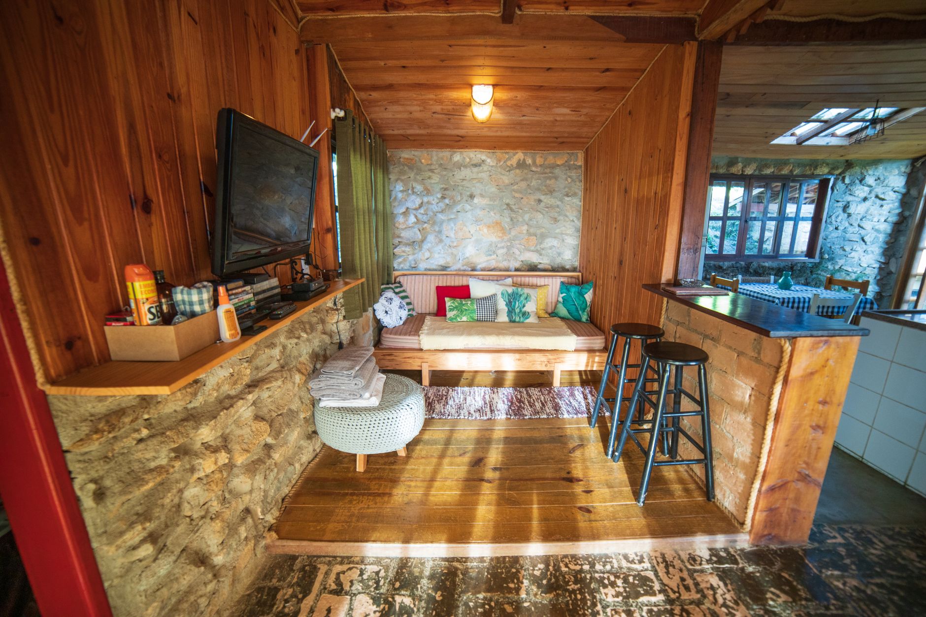 Interior of rustic house with counter placed near sofa with cushions and TV hanging on wooden wall near various supplies