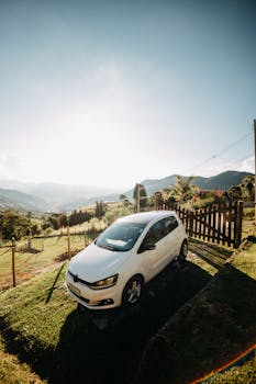 A white car parked in a vibrant, sunny countryside setting with hills and greenery.