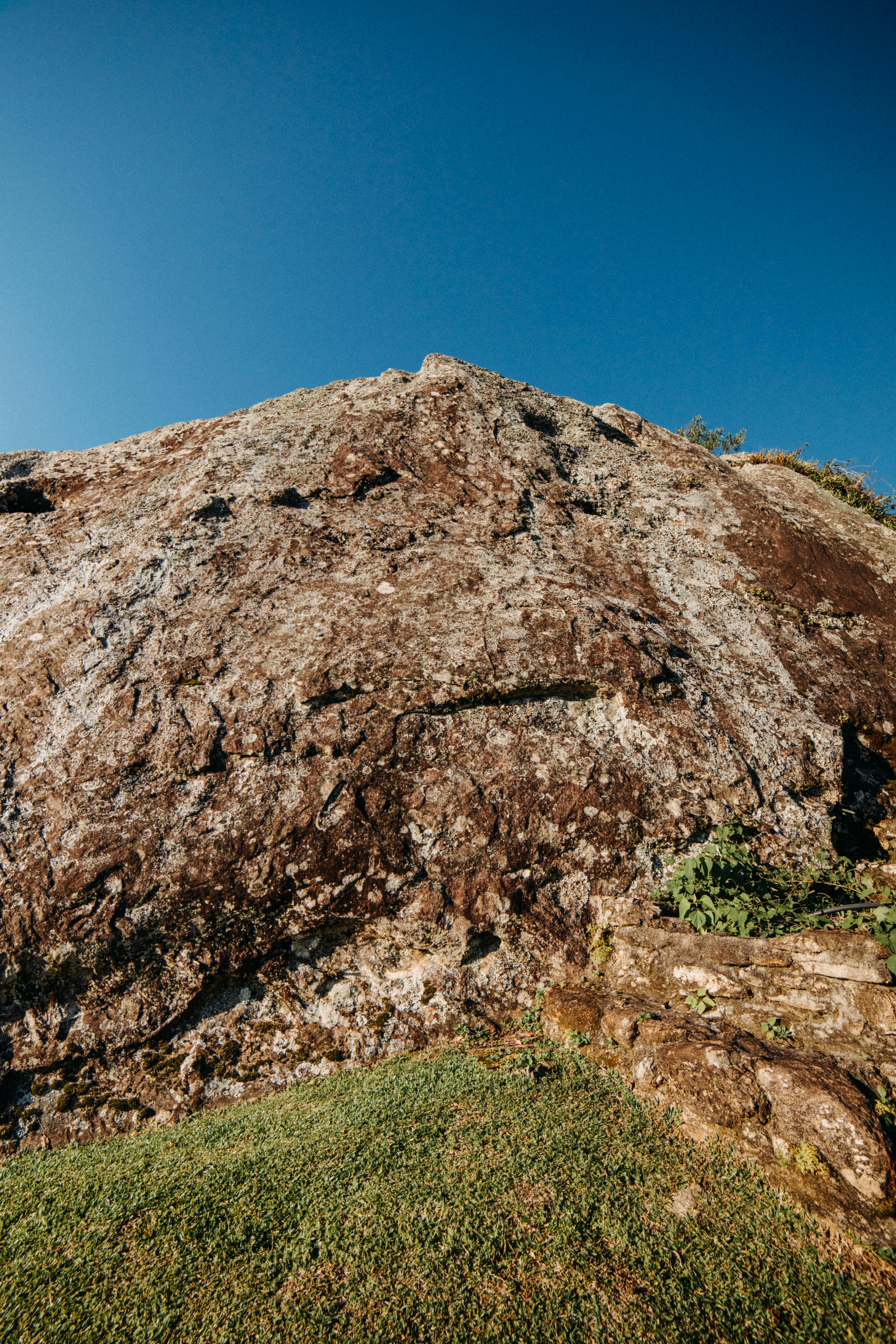 Rocky mountain with rough surface on grassy terrain against clear cloudless blue sky in suburb area on sunny summer day