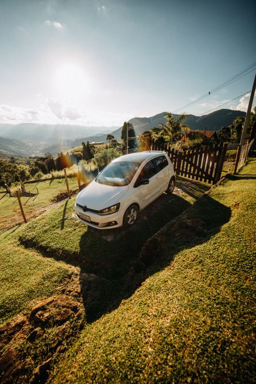 Free Modern white automobile parked on grassy ground near wooden fence against mountain ridge in suburb area on sunny summer day Stock Photo