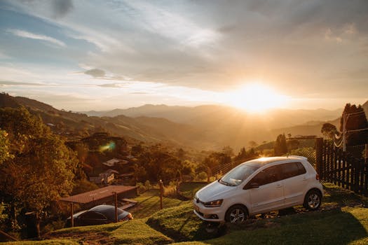 A white car parked on a hill with a stunning mountain sunset view.