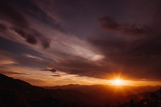 Breathtaking view of the sun setting over rolling mountains with dramatic clouds.