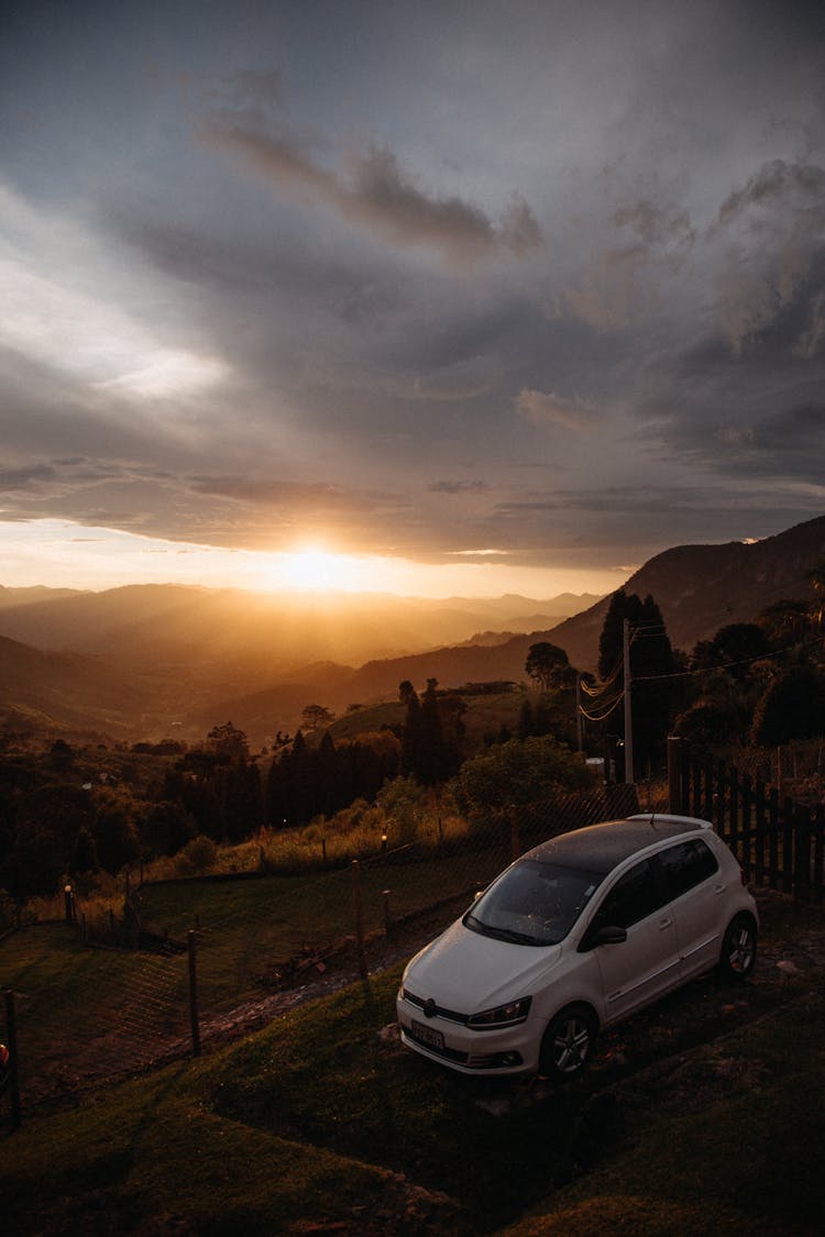 Car Parked In Front Of A Gate On A Hill At Sunset 