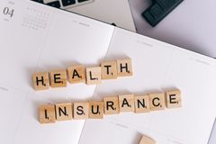 Scrabble tiles spelling 'Health Insurance' on a calendar, with laptop and stationery.