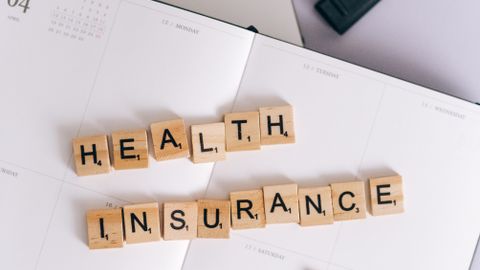 Scrabble tiles spelling 'Health Insurance' on a calendar, with laptop and stationery.