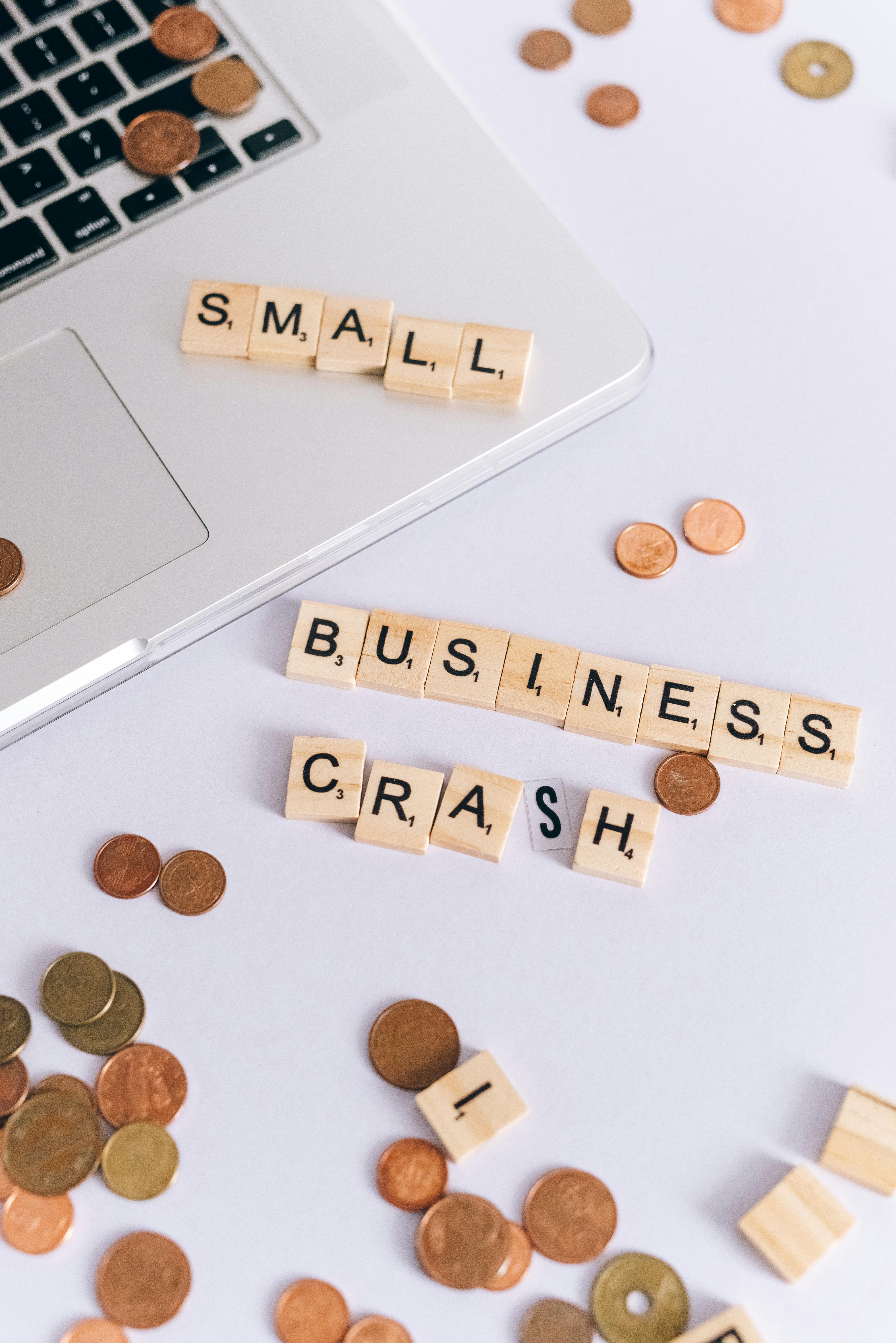 coins scattered around a sign saying small business crash lying on a laptop and white surface