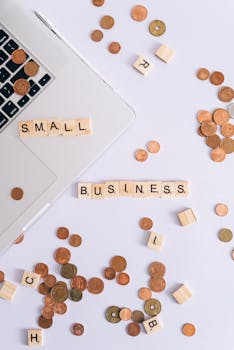 Flat lay of coins, Scrabble tiles spelling 'small business', and laptop, perfect for finance or entrepreneurship themes.