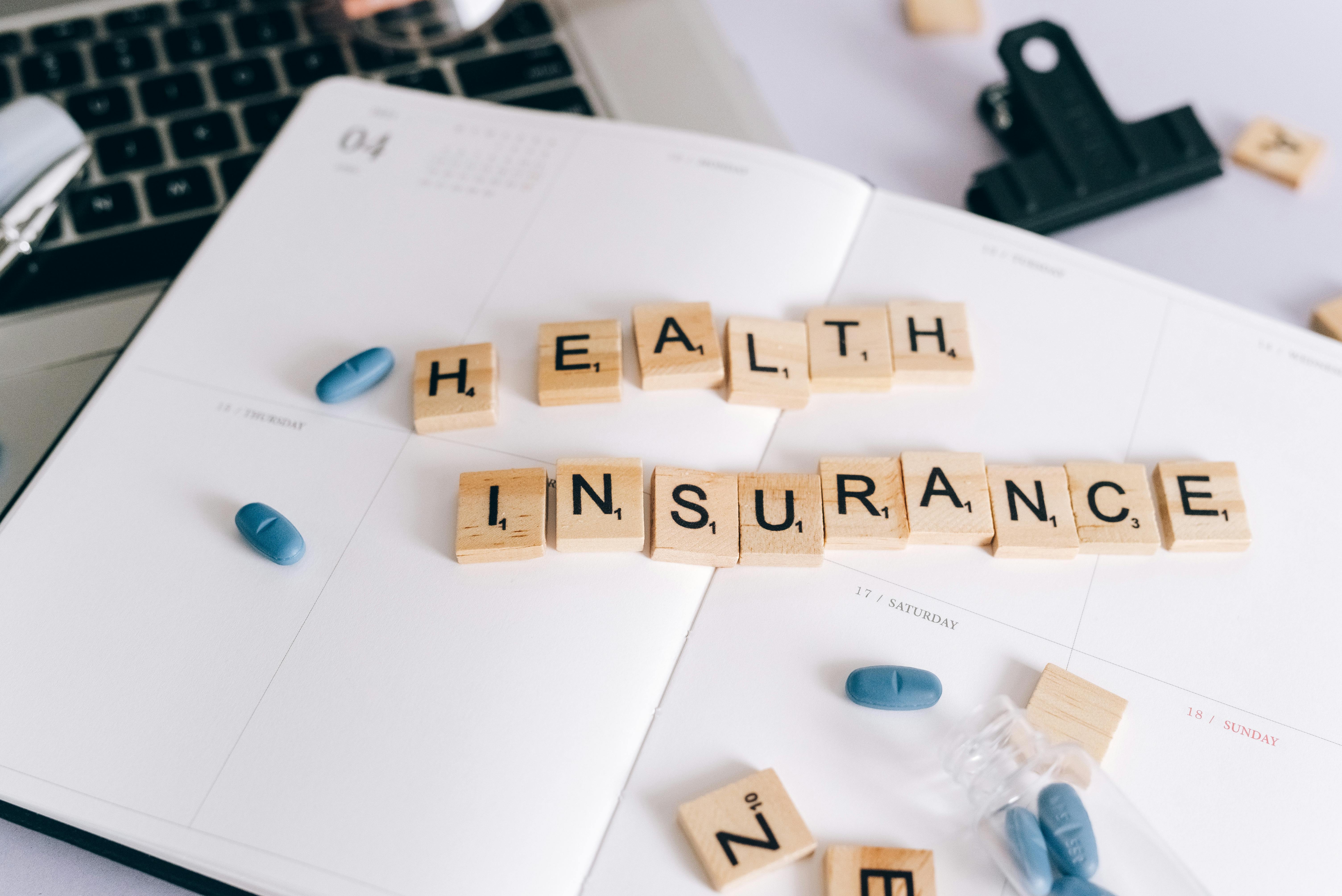 Health insurance written with Scrabble tiles on a calendar with blue pills and planner