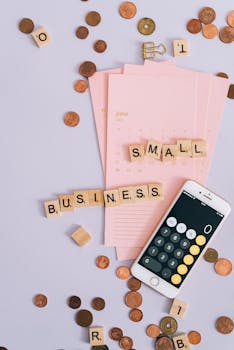 Flat lay with coins, smartphone, and 'SMALL BUSINESS' tiles on a planner.