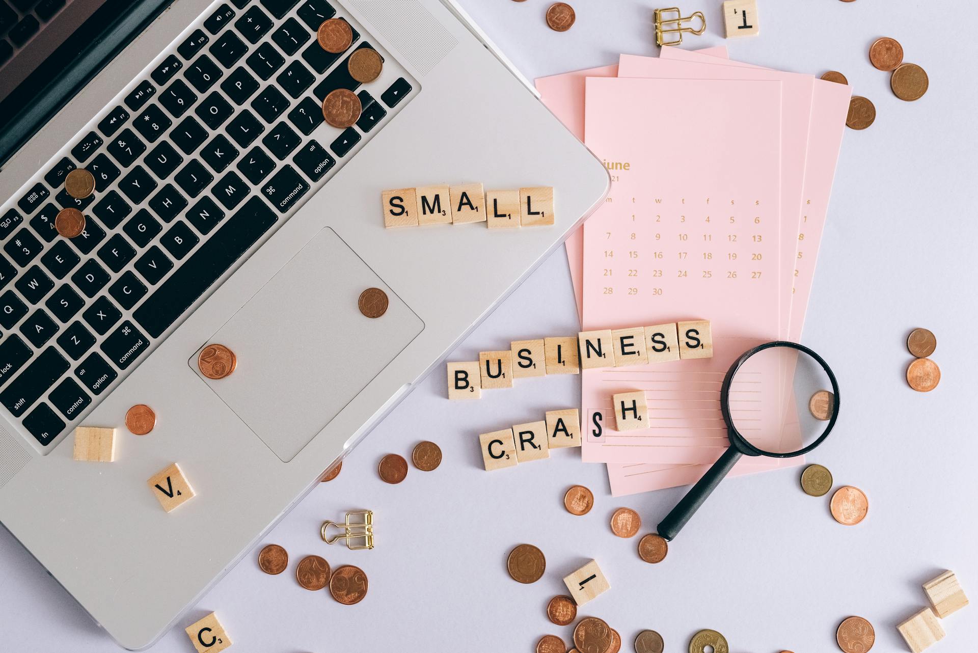 Flatlay of a laptop, coins, and scrabble tiles spelling 'small business crash'.