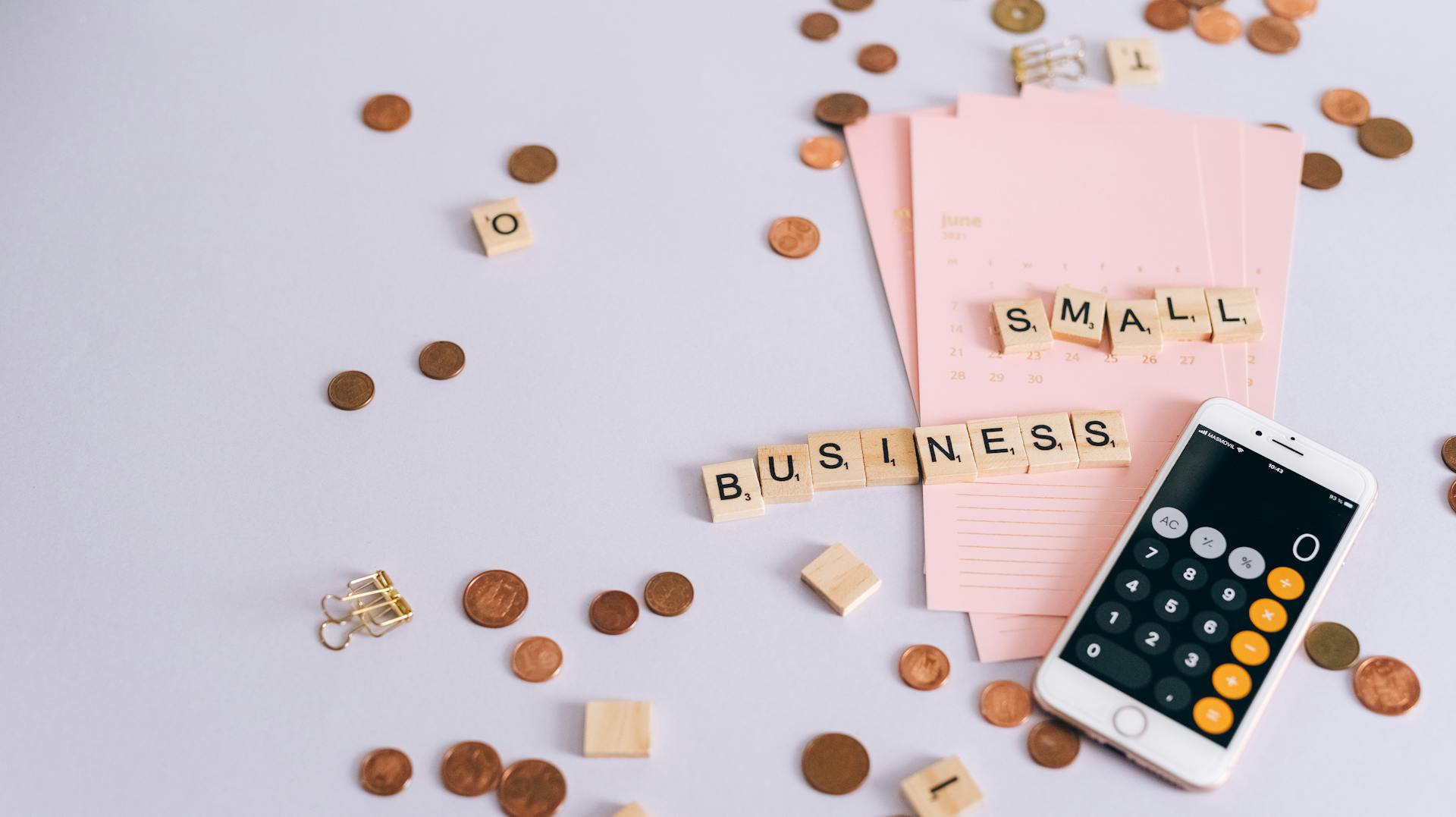 Flat lay image of small business finance concept with coins, calendar, and smartphone calculator.