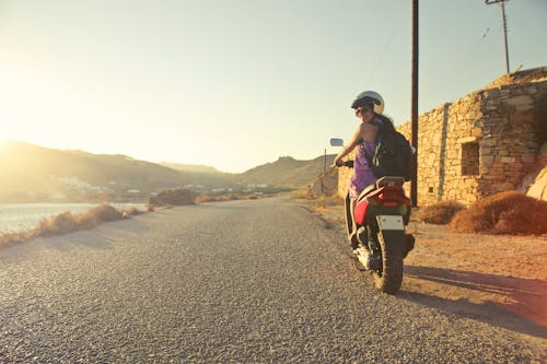 Reitender Motorroller Der Frau, Der Auf Asphaltstraße Während Sonnenaufgang Reist