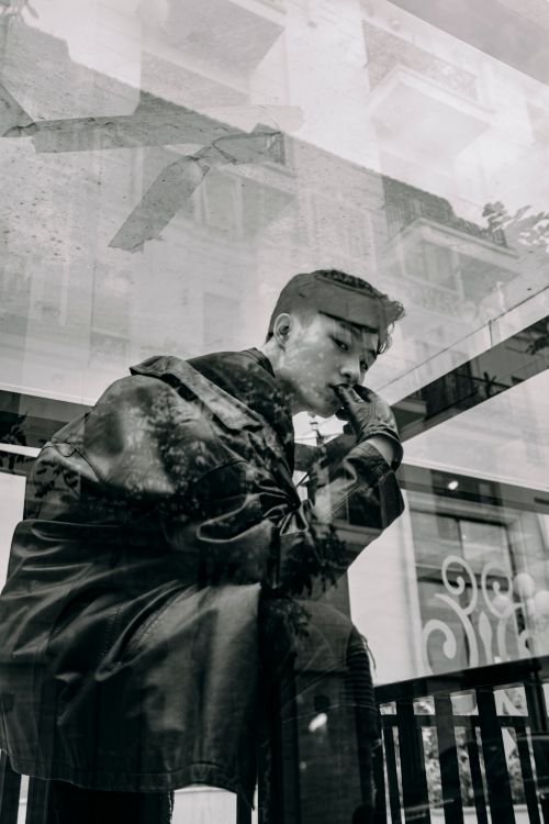 Free Low angle black and white through glass wall side view of stylish ethnic male in leather jacket looking at camera outdoors Stock Photo
