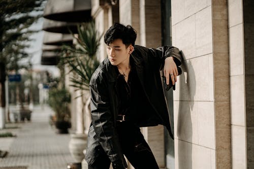 Free Unemotional stylish Asian male wearing black leather jacket standing confidently on modern city street and looking away Stock Photo