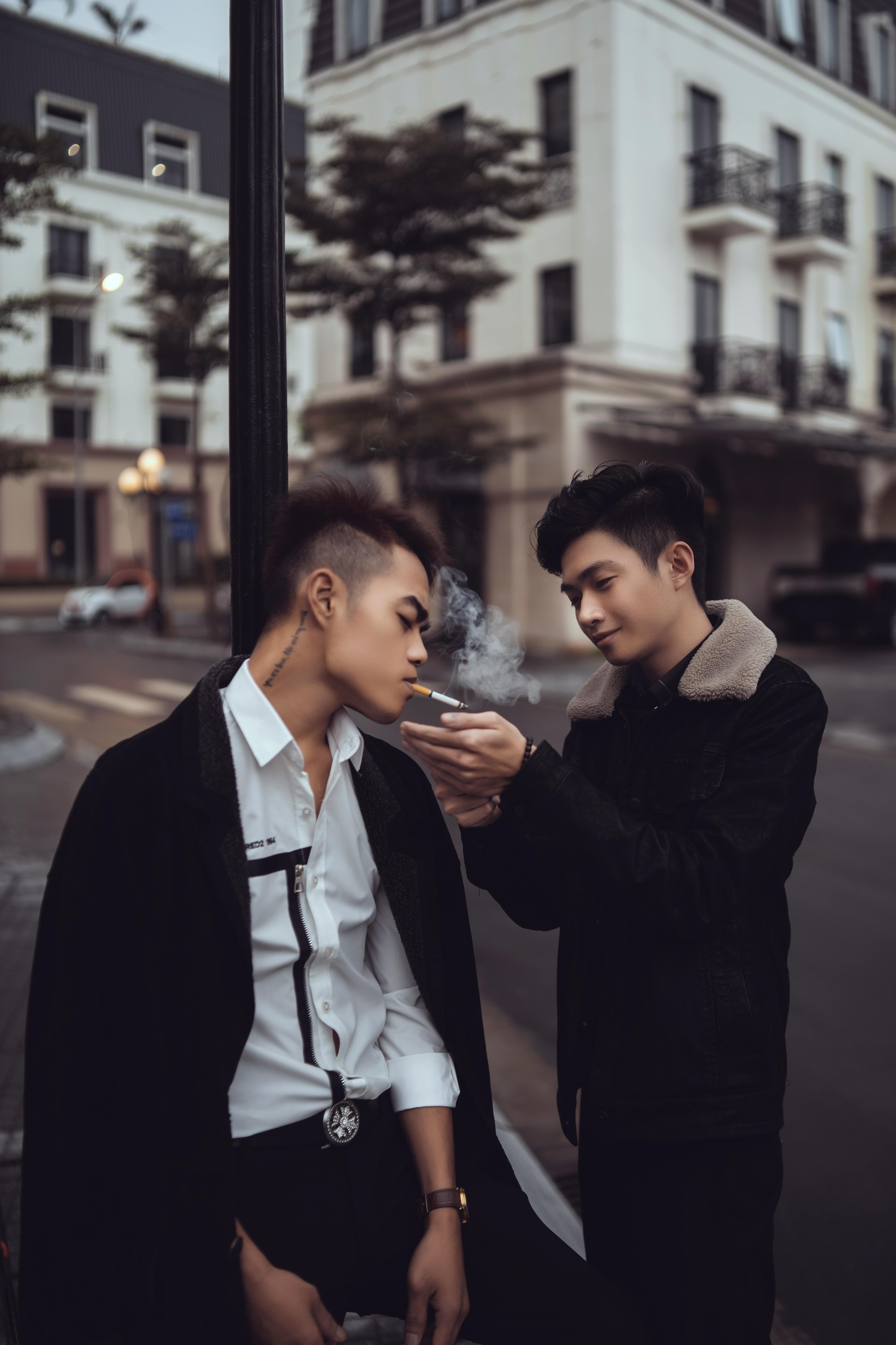 young asian man lightening cigarette for friend on street