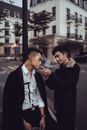 Young content Asian man giving light to smoking friend while standing together on street