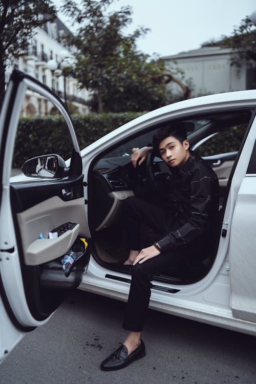 Free Full body confident young Asian male in black stylish wear sitting in modern posh car drivers seat and looking at camera Stock Photo