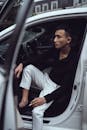 Stylish young Asian guy smoking while sitting in modern car with opened door