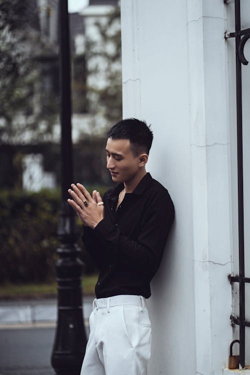 Side view of young fashionable Asian male millennial in classy outfit standing near building with white walls on city street