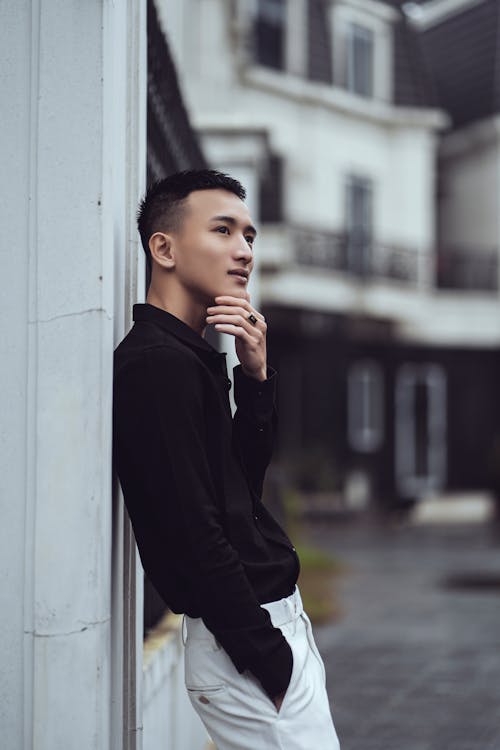 Stylish ethnic young man touching chin and looking away on street