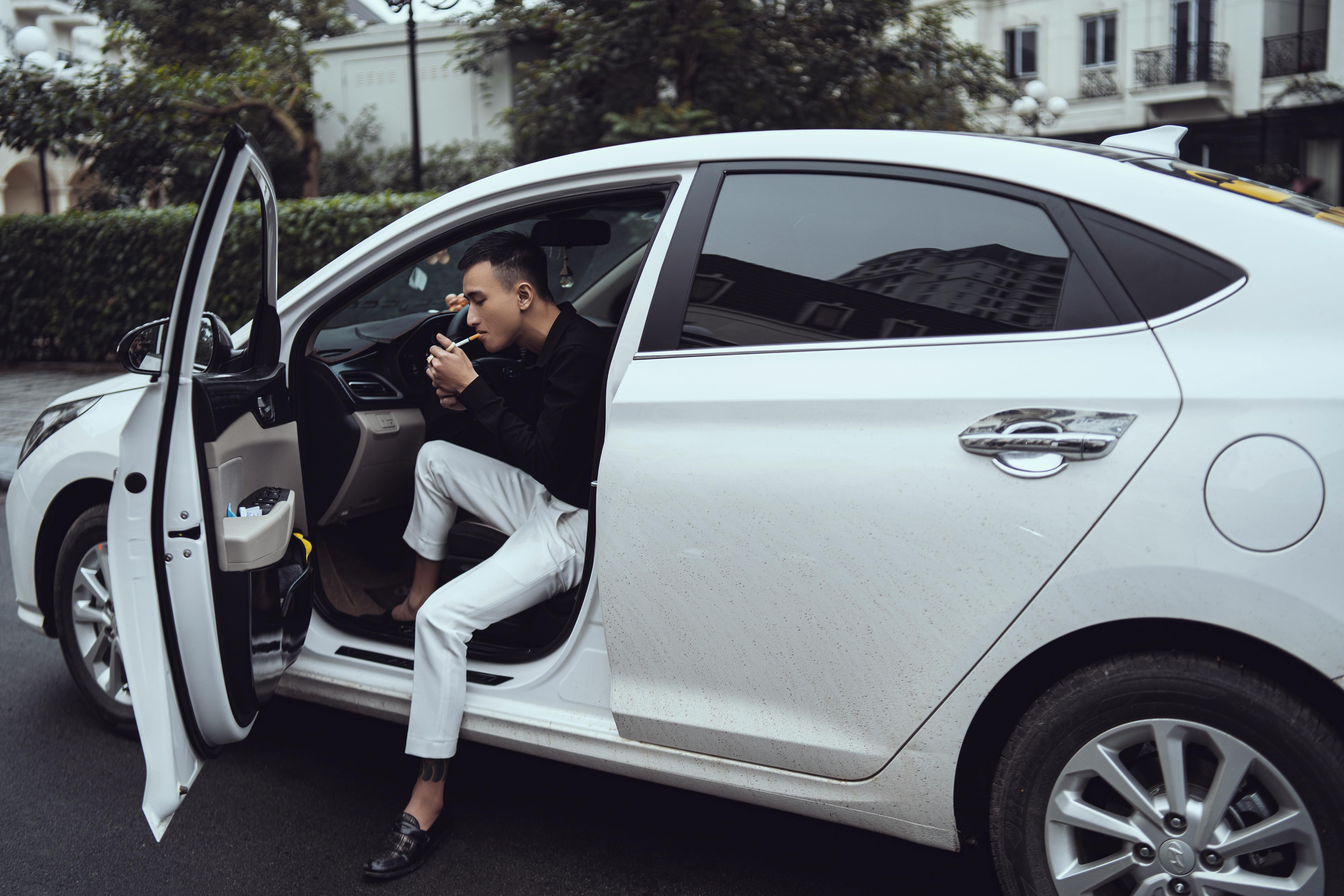 trendy young ethnic male driver smoking cigarette in contemporary car