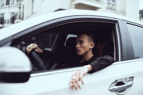 Free Side view of young concentrated Asian male millennial with cigarette in hand driving modern car in city Stock Photo