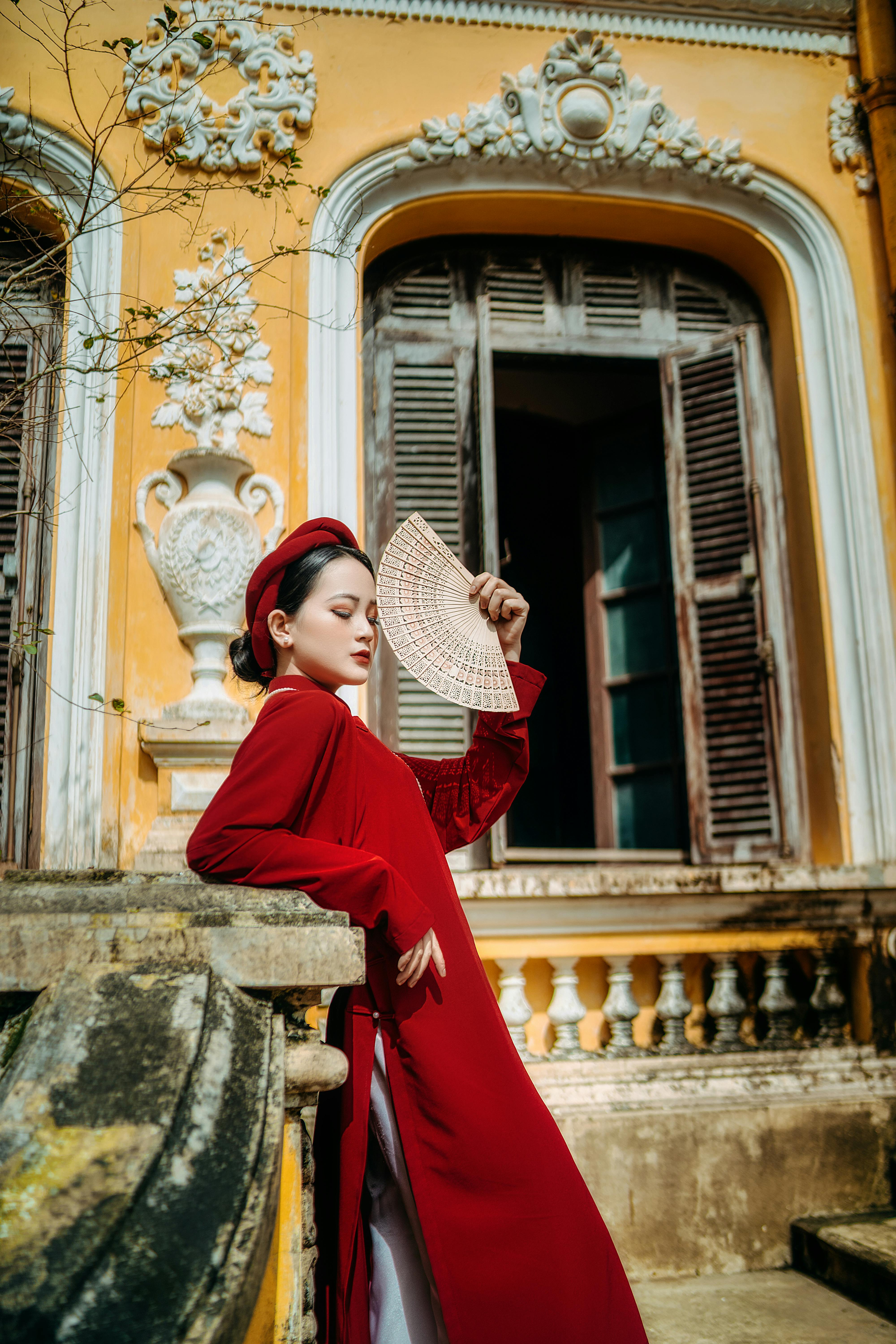 trendy asian woman with hand fan standing outside historic building
