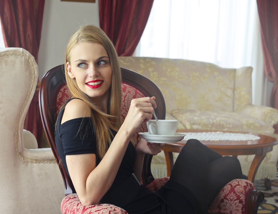 Woman in Black Cold-shoulder Dress Holding Tea Cup With Saucer