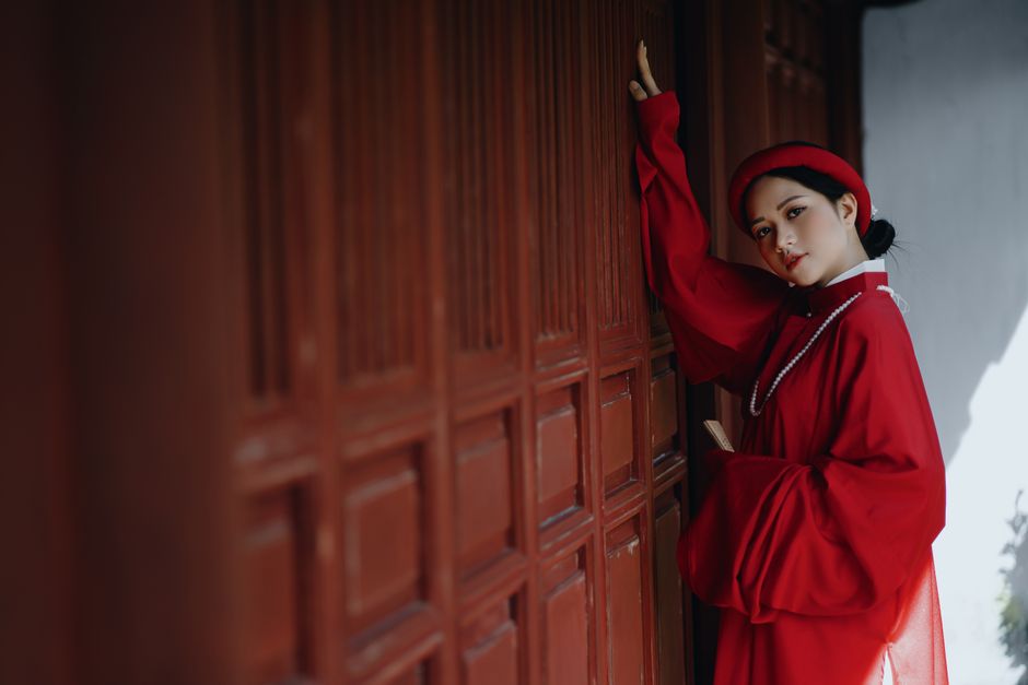 Asian woman in vintage red clothes standing against a wooden doorway.