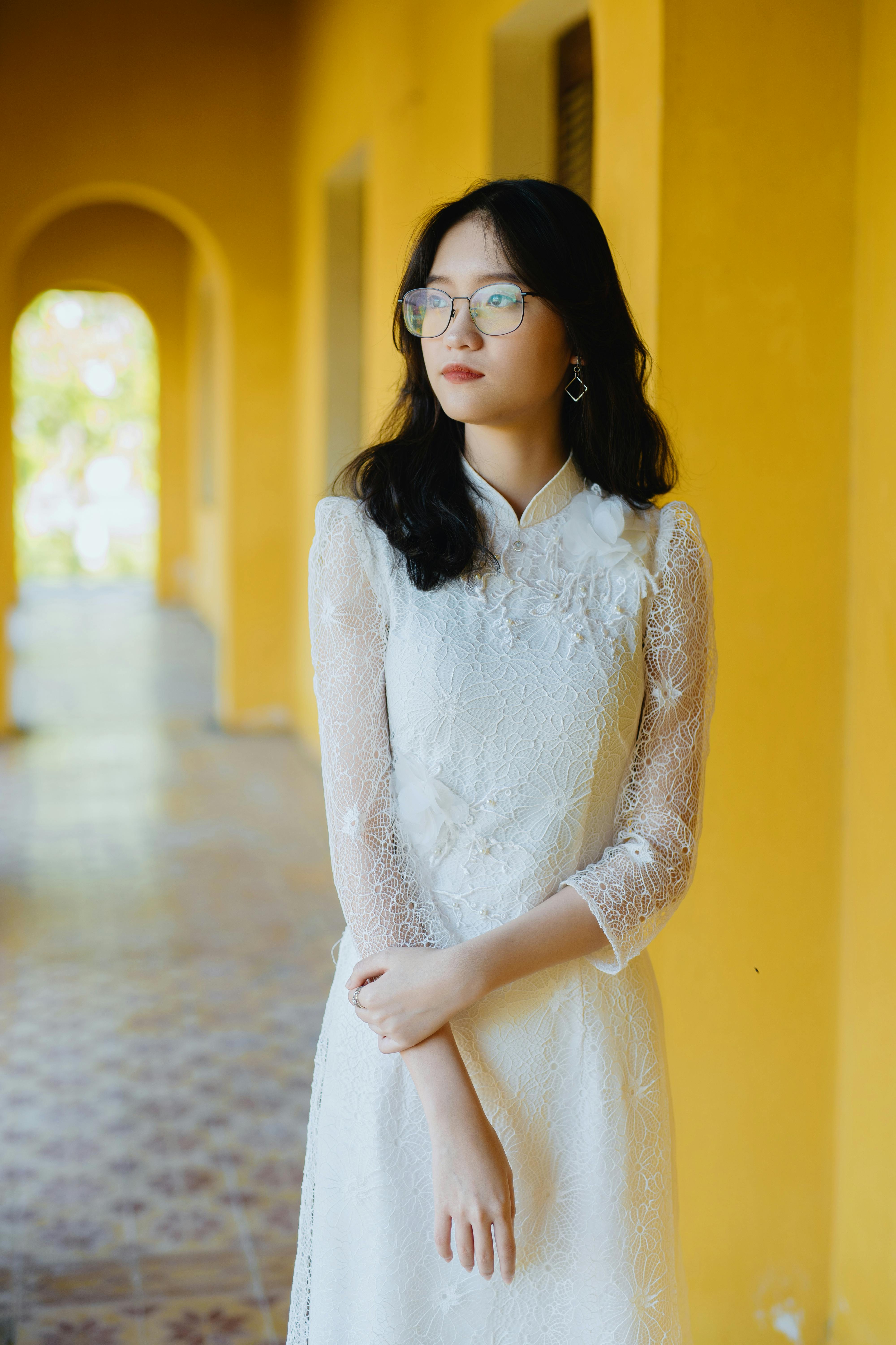 Elegant woman in white lace dress standing by an arched yellow hallway, evoking a serene mood.