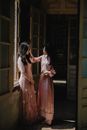 Full body attractive sensitive female wearing chic pink gown touching female friends face while standing together in mansion hallway