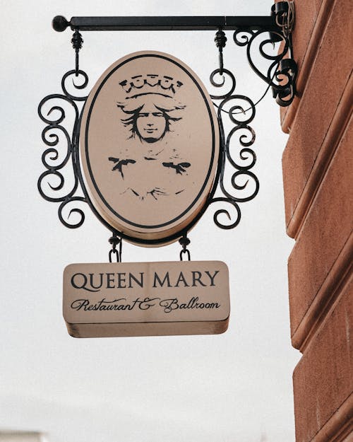Low angle of old signboard under portrait of queen hanging on brick building wall under gray sky in daytime in city street