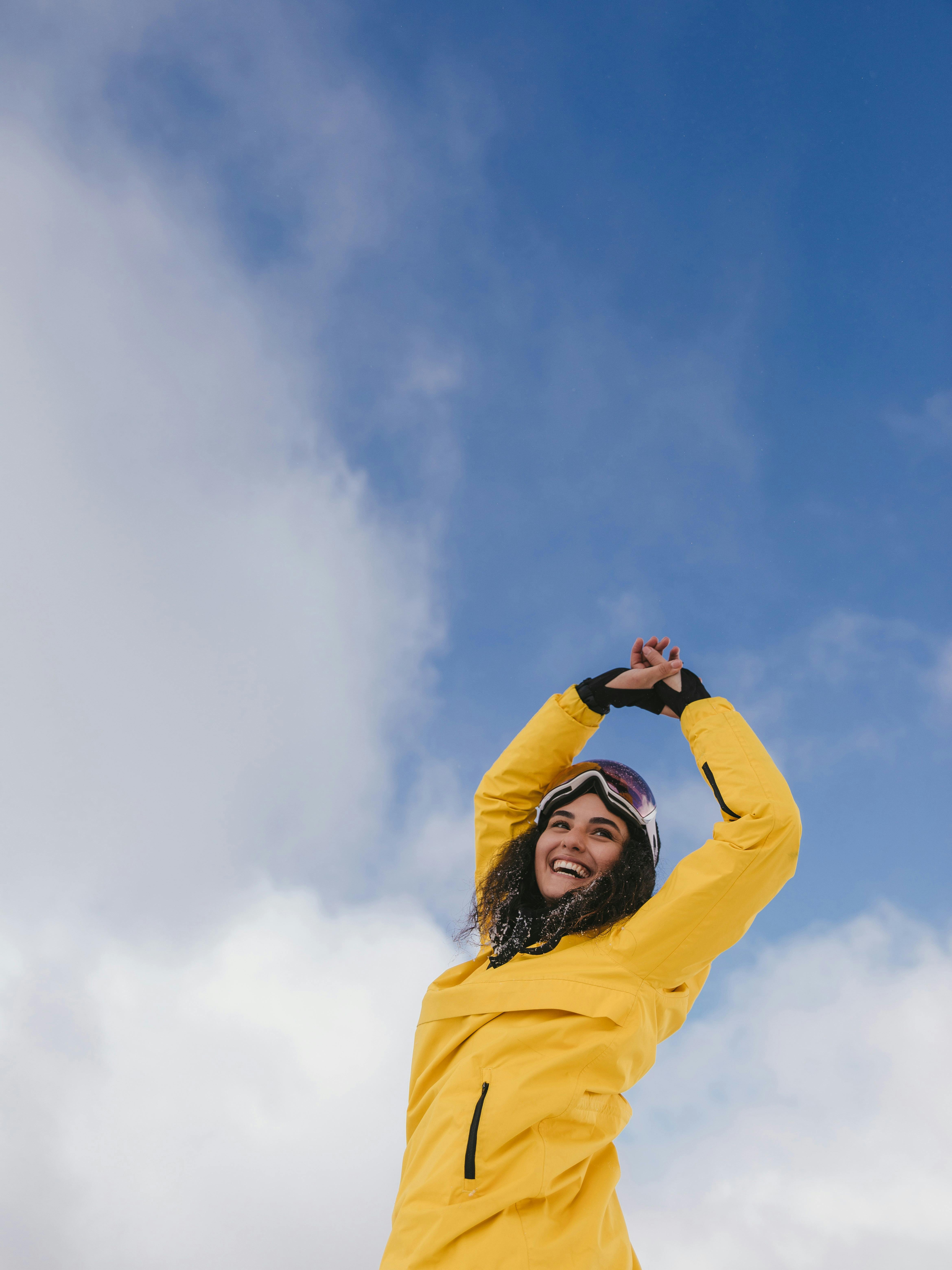 Prescription Goggle Inserts - Smiling woman in yellow jacket enjoying a snowy day with blue sky and clouds.