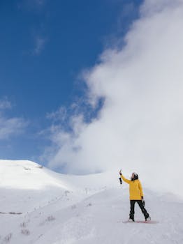 A woman in a yellow jacket enjoys skiing on a snowy mountain under a clear blue sky.