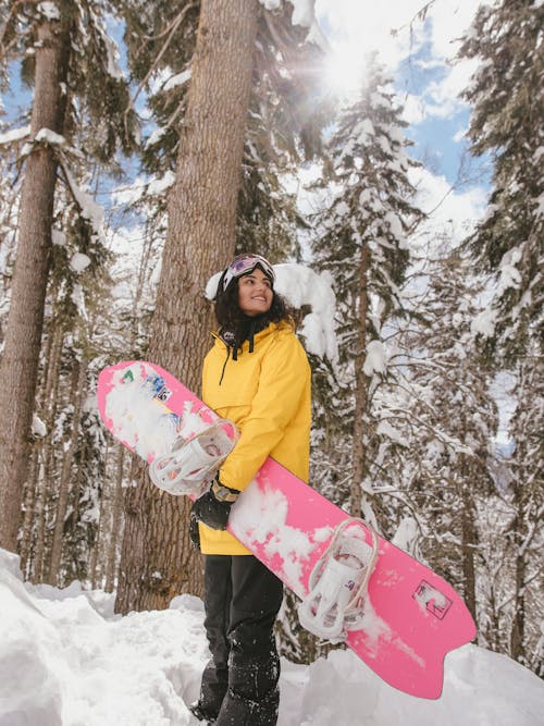 A Woman in Yellow Jacket Standing on a Snow Covered Ground while Holding a Snowboard