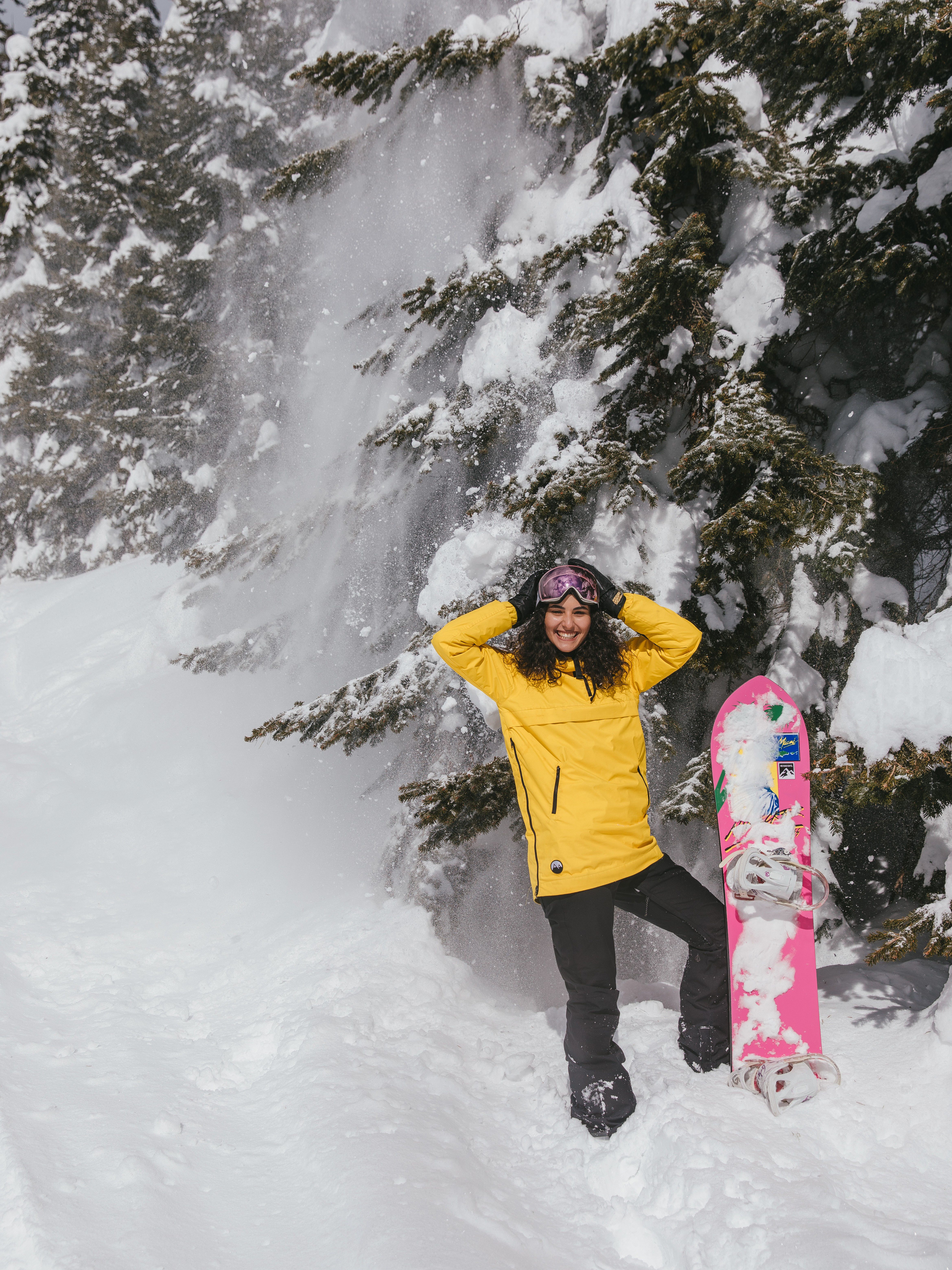Smiling woman in yellow jacket snowboarding in a snowy winter landscape with fir trees.