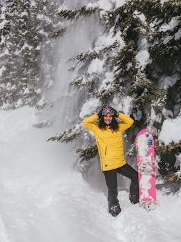 Smiling woman in yellow jacket snowboarding in a snowy winter landscape with fir trees.