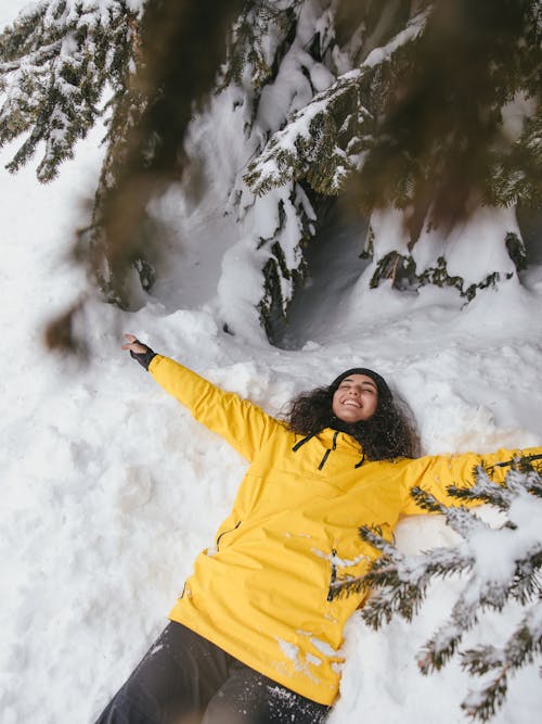 Woman in Yellow Jacket Lying Down on a Snow Covered Ground