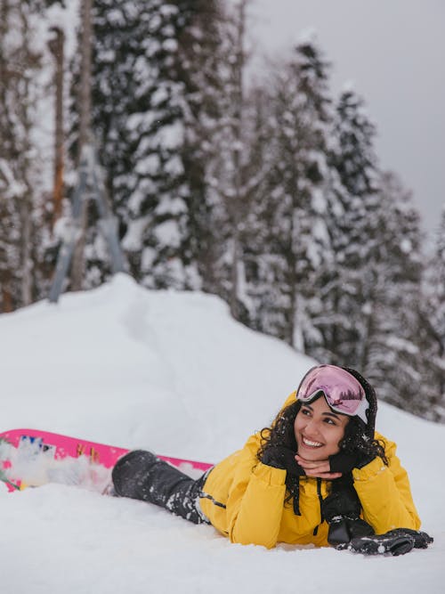 Smiling Woman in Yellow Winter Jacket Lying Down on the Snow-Covered Ground