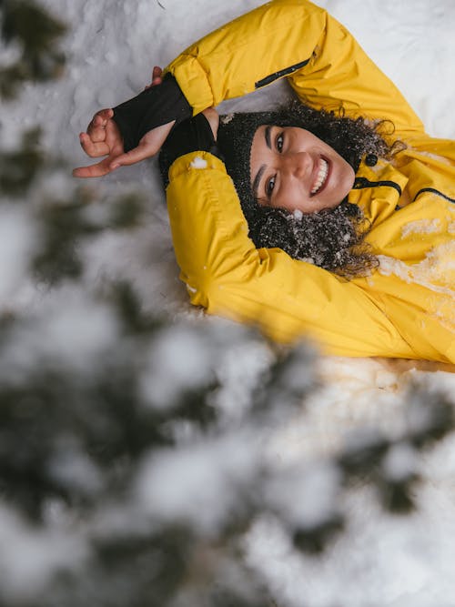 A Woman Lying on a Snow Covered Ground while Wearing a Yellow Jacket