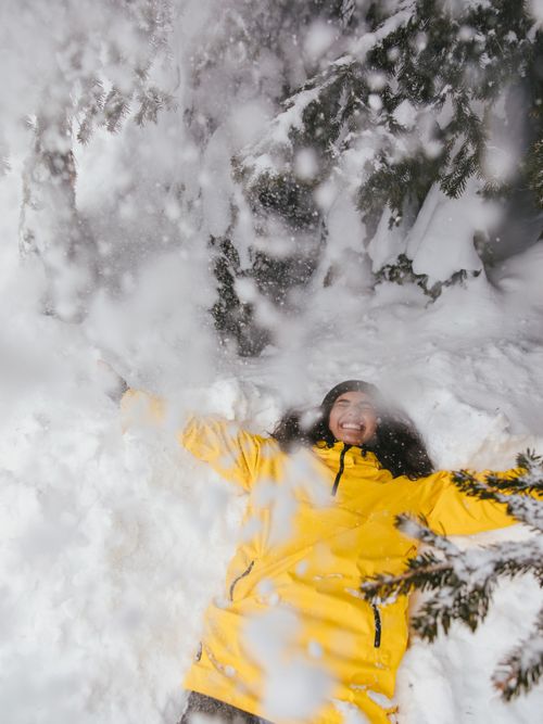 Free A woman in a yellow jacket joyfully playing in fresh snow, captured outdoors in winter. Stock Photo