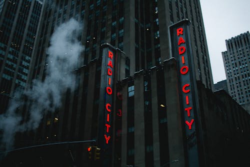Free From below of exterior of modern multistory commercial building with red neon signboard against cloudy sky in New York City Stock Photo