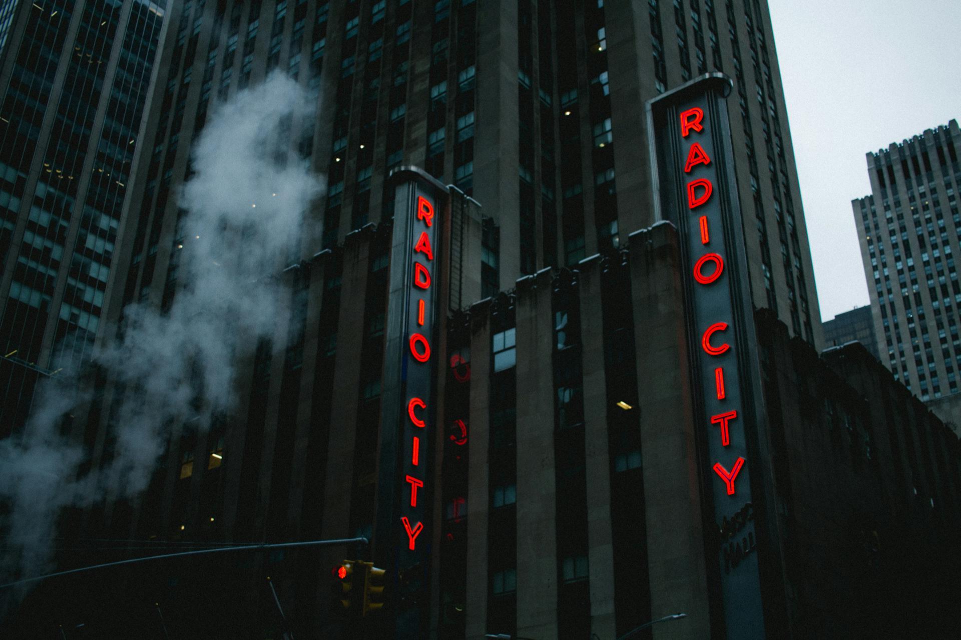 From below of exterior of modern multistory commercial building with red neon signboard against cloudy sky in New York City