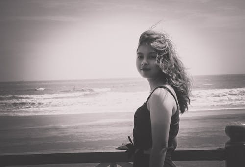 Grayscale Photo of Woman Wearing Tank Top Standing Near Seashore