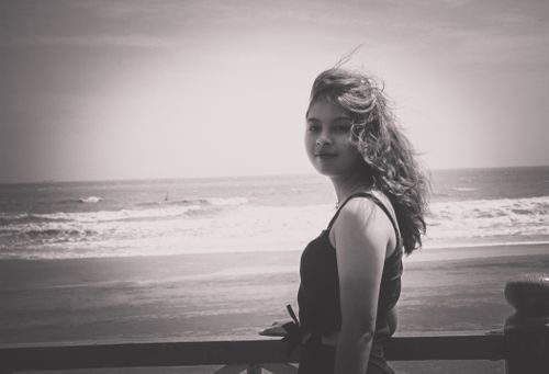 Free Black and white photo of a woman on a windy beach, with waves in the background. Stock Photo