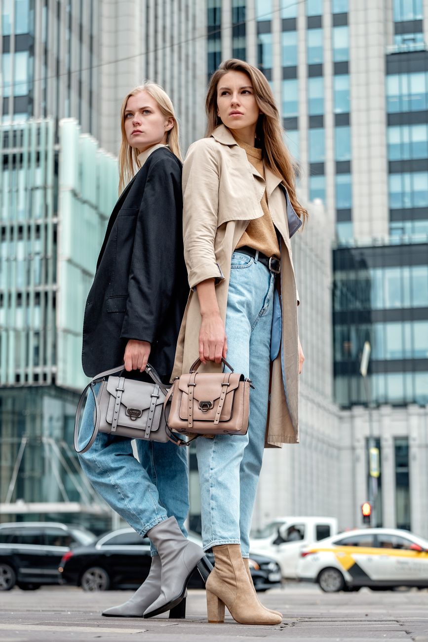 Stylish young women posing with handbags on a city street, showcasing modern urban fashion.