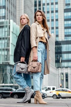 Stylish young women posing with handbags on a city street, showcasing modern urban fashion.